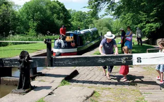 Family push a lock gate closed as a narrowboat prepares to go down the lock
