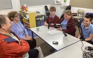 3 school children interviewing 2 adults using microphones