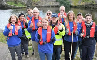 Group of volunteers pose with thumbs up in front of a canal