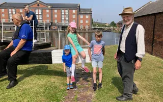 A man in Victorian costume stands by a lock gate with three young children
