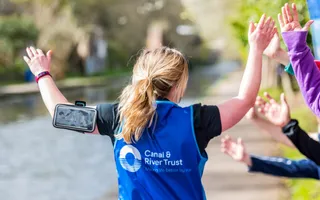 Woman running with her arms raised, wearing a 'Canal & River Trust' vest