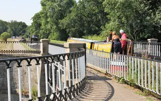 Boat passes over a small aqueduct with moored narrowboats in the distance