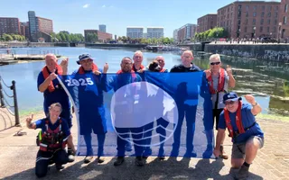 Group of people holding a blue flag infront of a body of water
