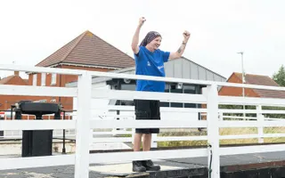 Person standing on a bridge holding hands up and smiling.