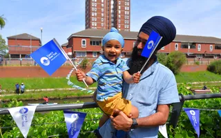 Child in father's arms waving Canal & River Trust flags on bunting-lined towpath