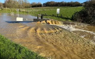 Vast amounts of muddy water rushes underneath a lock gate and bursts the canal banks
