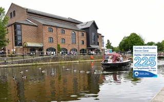 A boat on the water at Brecon Basin with a large theatre building in the background