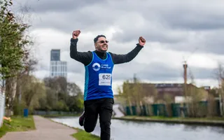 A man celebrating with his arms in the air as he runs along the towpath
