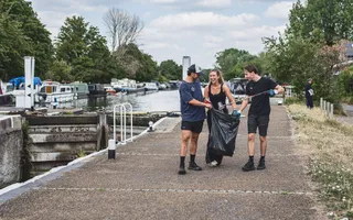 Two men and one woman walk along the towpath next to a lock gate, holding a bin bag and litter pickers and smiling.