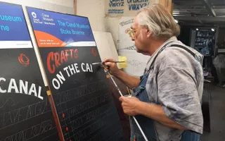 Man with a paint brush painting letters onto a black board