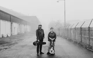 Black and white photo of two people standing on road holding instruments.