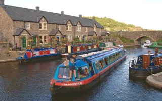 Blue trip boat named 'Dragonfly' passes moored boats and brick-built houses at Brecon Basin