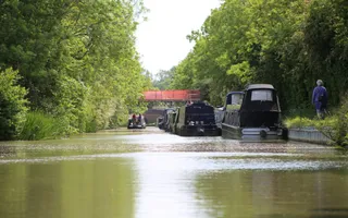 Boats are moored next to the towpath to the right, whilst another boat drives away from the camera up the canal