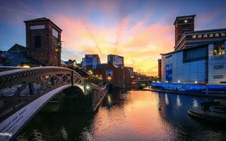 The sun rises over central Birmingham, reflecting the surrounding buildings in the canal.