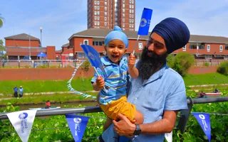 Father holds son waving flags by the canal