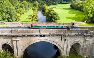 Aerial view of a narrowboat crossing an aqueduct over a river and surrounded by verdant fields.