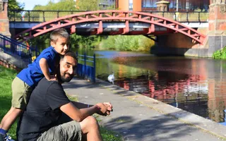 Boy leans against father sitting next to the canal in the sun