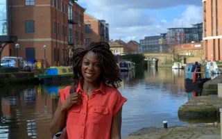 Woman smiles at camera in front of a canal lined with moored boats and buildings