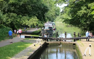 People walking along the towpath beside a lock gate in the bright sunshine