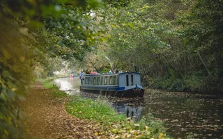 Blue narrowboat cruising canal in autumn with passengers on the back