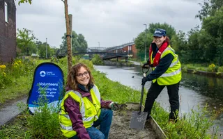 Two volunteers in high vis jackets gardening on the canal towpath