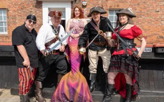 Group of people dressed as pirates sitting on a wall with person dressed as a mermaid in the middle