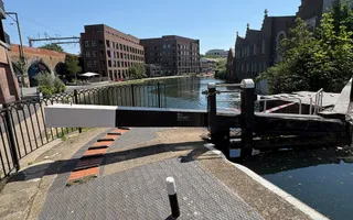 A black and white lock gate stretches across a canal with concrete towpaths either side