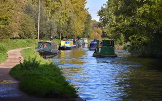 A gravel towpath follows the curve of a canal with multiple boats moored along the side.