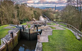 Looking down a steep flight of staircase locks at the calm canal with an industrial factory and chimney on the horizon.