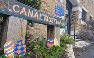 Old wooden sign saying 'CANAL MUSEUM' with easter egg cut outs around it.