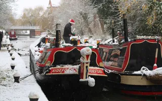 Snow covers the towpath and two boats moored double breast as walkers pass