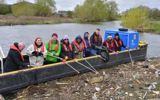 A group of corporate volunteers on a Canal & River Trust work boat hold litter pickers to collect plastic rubbish from the water.