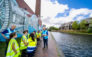 Wide shot of a blue boat on the canal with children in high vis walking on the left towpath