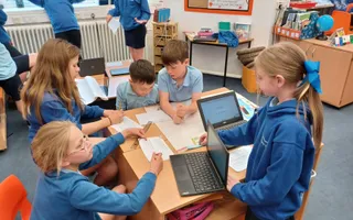 School children sitting around laptops on a small table