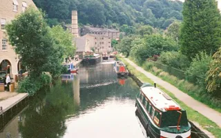 Narrowboats moored along the canal at Hebden Bridge, with buildings on the offside and a factory chimney in the distance