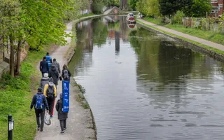 A group of adults walk away from the camera along the towpath, which runs parallel to the canal