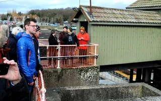 A group of people standing by a fence next to a green building on stilts