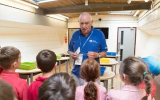 Older man in blue top teaching children in a classroom