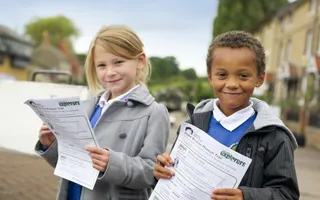 Two children in school uniform stand by a lock beam holding Canal & River Trust worksheets for Exporers