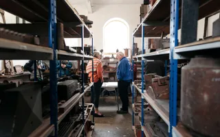 A volunteer talks to a member of the public in a room filled with shelves laden with historic pots, beams, and other parts of canal infrastructure.