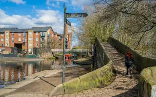 Person walks over a bridge at a three-way canal junction with a sign pointing to Marple, Whaley Bridge, and Macclesfield.