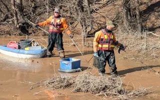 two men standing in brown water with fishing equipment