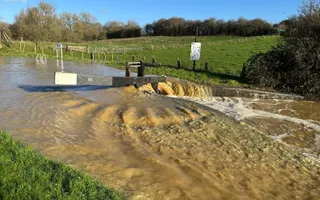 A flooded canal overtops a lock gate and surrounding towpath.