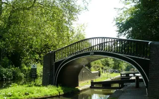 A black and white metal bridge in front of a single lock on a sunny day.