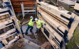 Engineers in high vis and helmets push a newly built lock gate into place in a drained lock pound