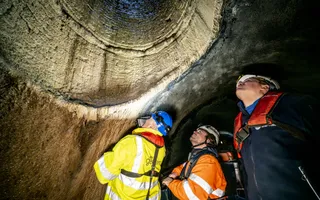 Three people in PPE looking above at a wall inside a tunnel