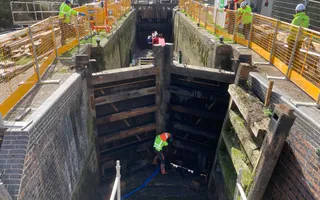 Wide shot of a drained canal with lock gates and a worker at the bottom