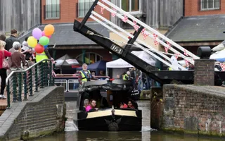 Narrowboat passes under swing bridge decorated in bunting and balloons