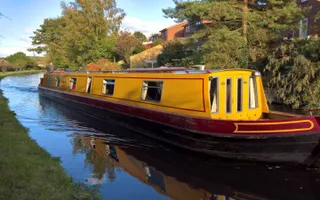 A narrowboat moves along the canal, surrounded by trees