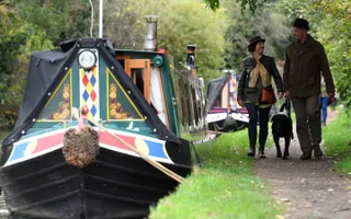Couple walk their dog passed moored narrowboats